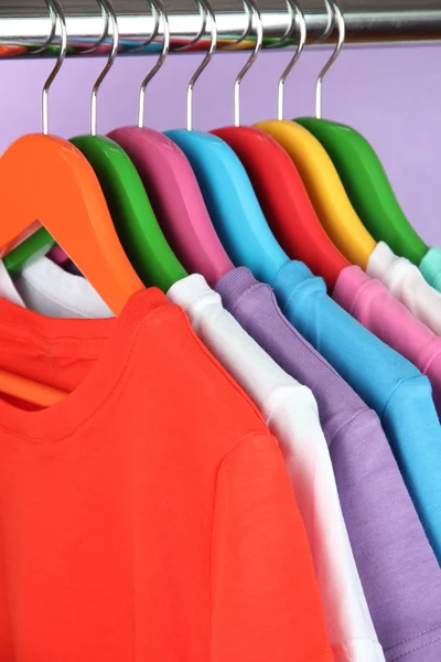 Camisas diferentes em cabides coloridos no fundo roxo — Fotografia de Stock