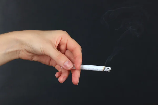 Mulher mão segurando cigarro com fumaça, isolado em preto — Fotografia de Stock