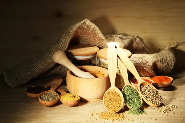 Assortment of spices in wooden spoons and jars, on wooden background — Stock Photo, Image