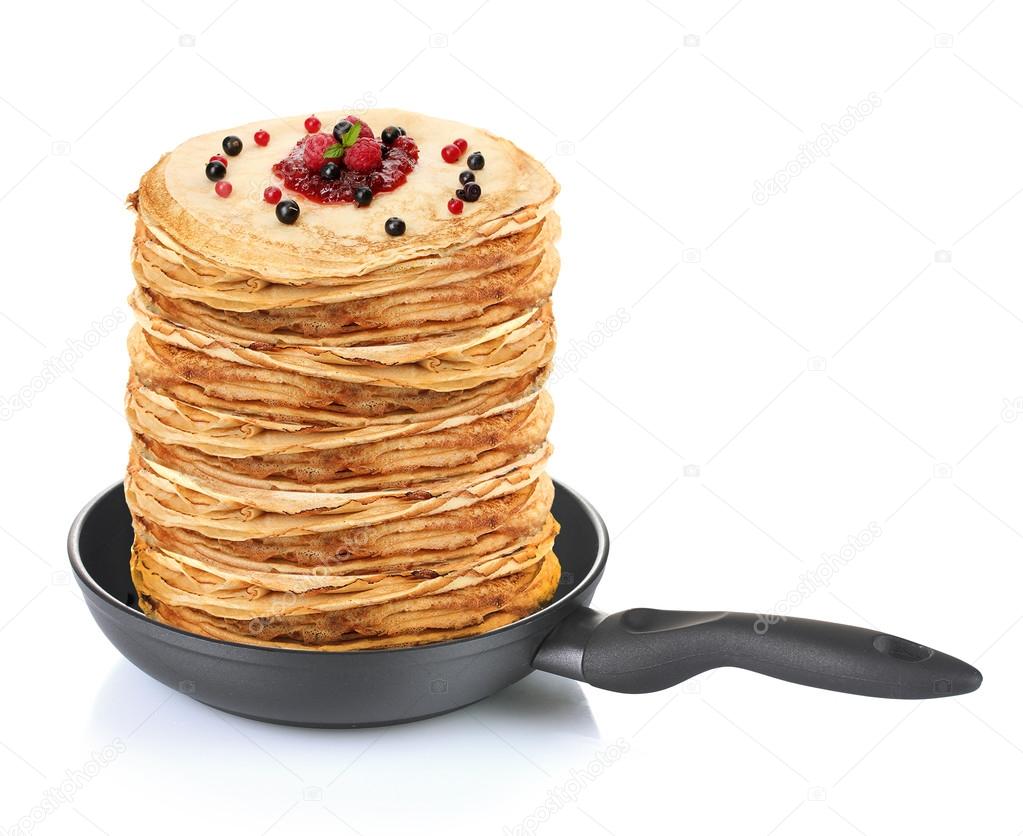 Large stack of pancakes with berries in frying pan isolated on white