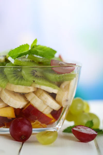 Salada de frutas saborosas em tigela de vidro, na mesa de madeira branca — Fotografia de Stock