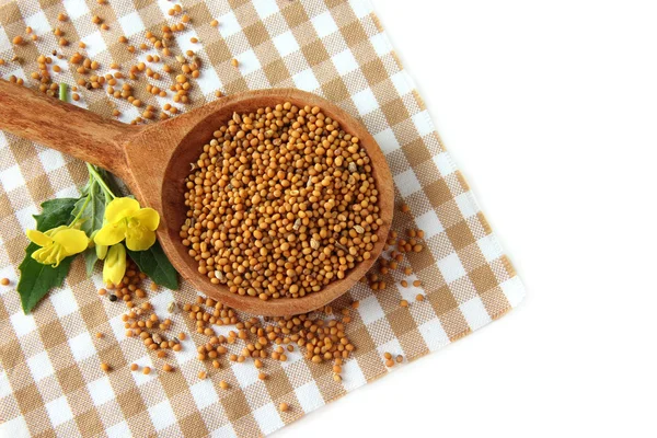 Mustard seeds in wooden spoon with mustard flower isolated on white — Stock Photo, Image