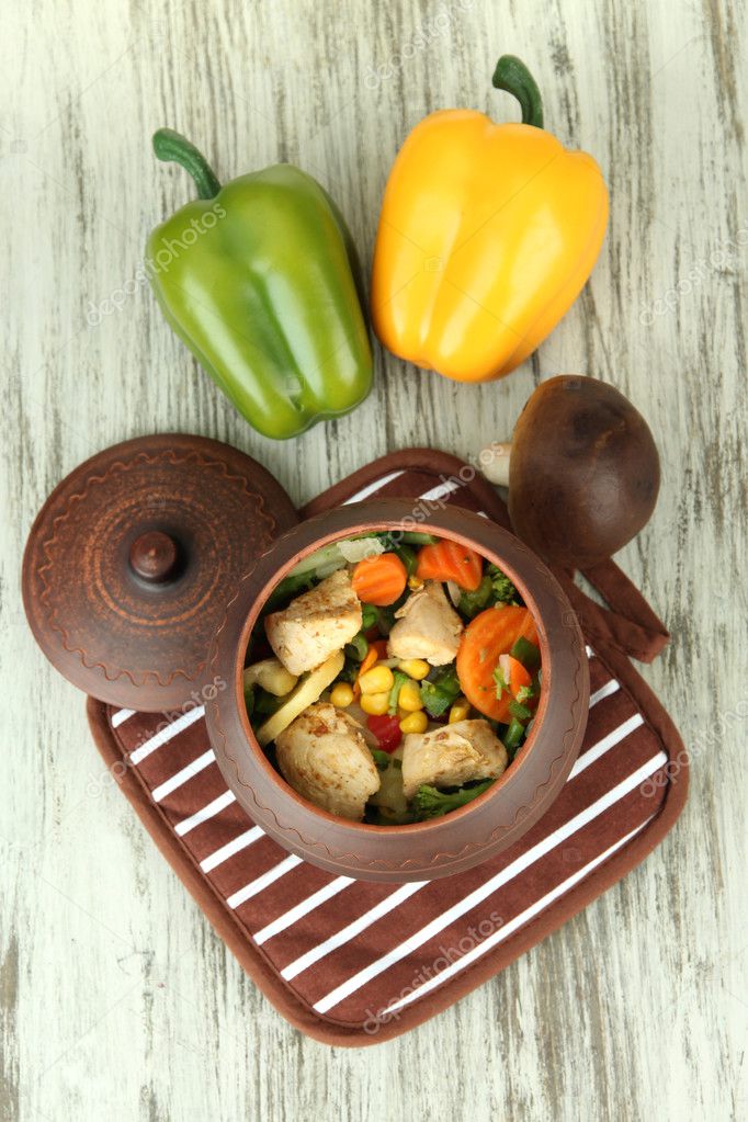 Baked mixed vegetable with chicken breast in pot on potholder, on wooden background