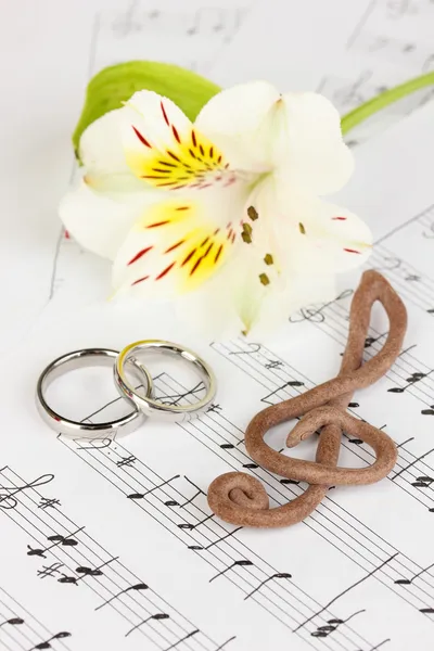 Treble clef, bloem en trouwringen op muzikale achtergrond — Stockfoto