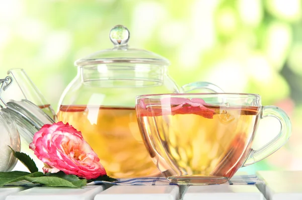 Konvice a šálek čaje z tea rose na ubrousek na dřevěný stůl na pozadí přírody — Stock fotografie