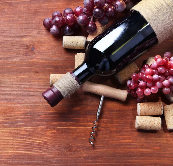 Láhev vína, vinných hroznů a zátky na dřevěné pozadí — Stock fotografie