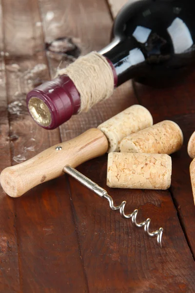 Corkscrew with wine corks and bottle of wine on wooden table close-up — Stock Photo, Image