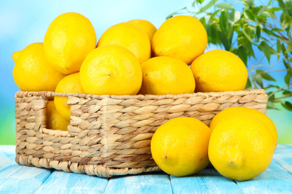 Ripe lemons in wicker basket on table on bright background