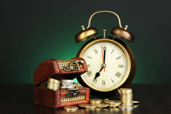 Antique clock and coins on wooden table on dark color background — Stock Photo, Image