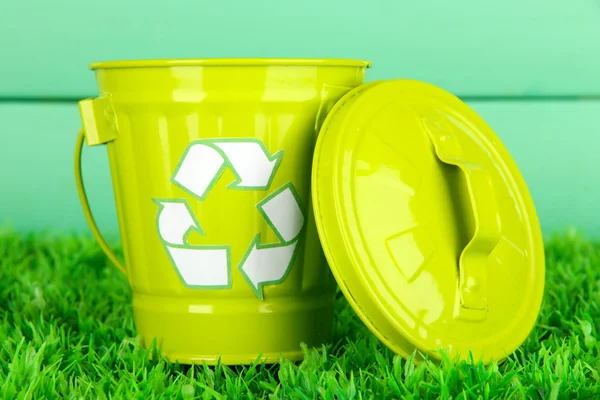 Recycling bin on green grass on color wooden background — Stock Photo, Image