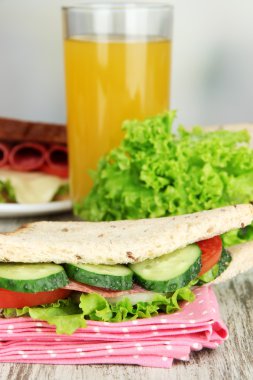 Lezzetli sandviç salam sosis ve parlak zemin üzerine ahşap masa üzerinde renkli peçete üzerinde sebze ve meyve suyu ile kompozisyon