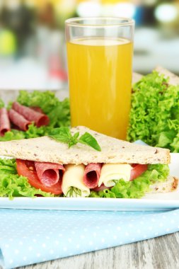Lezzetli sandviç salam sosis ve ahşap masa arka plan üzerinde renkli peçete üzerinde sebze ve meyve suyu ile kompozisyon