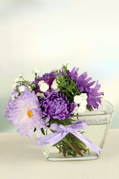 Beau bouquet de fleurs lumineuses en vase en verre, sur table en bois, sur fond lumineux — Photo