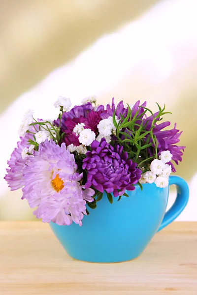Красивый букет ярких цветов в цветной кружке, на деревянном столе, на ярком фоне — стоковое фото