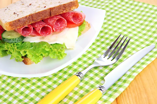 Lekkere sandwich met worst salami en groenten op witte plaat, op houten achtergrond — Stockfoto