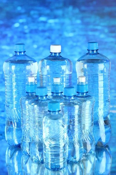 Agua en diferentes botellas sobre fondo azul —  Fotos de Stock