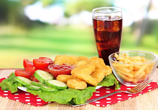 Fried chicken nuggets with french fries,cola,vegetables and sauce on table in park — Stock Photo, Image