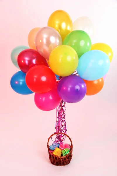 Many bright balloons and basket with gifts on purple background — Stock Photo, Image