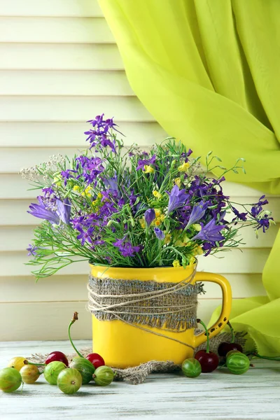 Krásnou kytici květin v poháru a bobule na dřevěný stůl — Stock fotografie