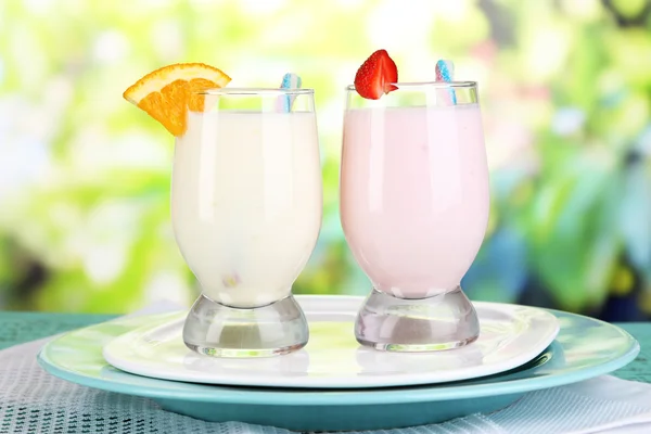 Delicious milk shakes with orange and strawberries on wooden table on natural background — Stock Photo, Image