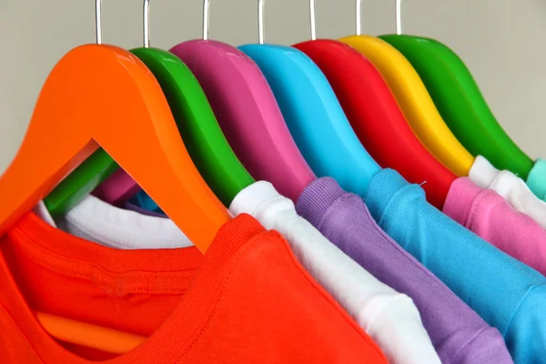 Camisas diferentes em cabides coloridos no fundo cinza — Fotografia de Stock