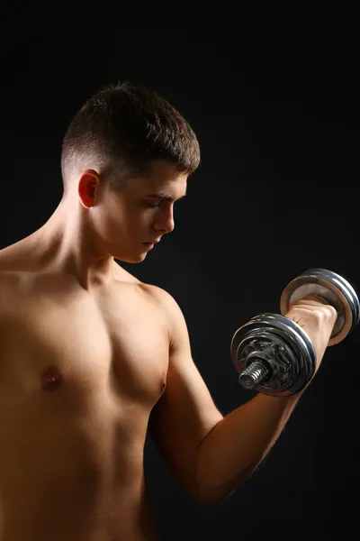 Guapo joven deportista muscular ejecutar ejercicio con mancuerna sobre fondo oscuro — Foto de Stock