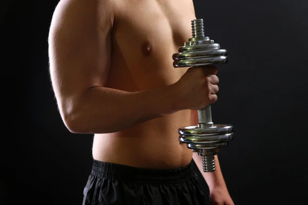 Handsome young muscular sportsman execute exercise with dumbbell on dark background — Stock Photo, Image