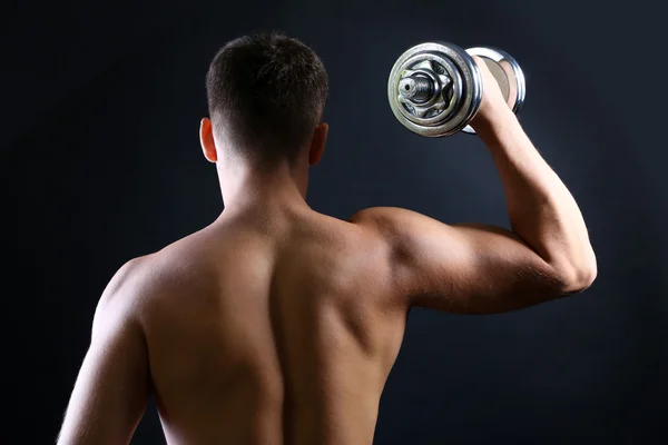 Knappe jonge gespierde sportman uitvoeren oefening met dumbbell op donkere achtergrond Stockfoto