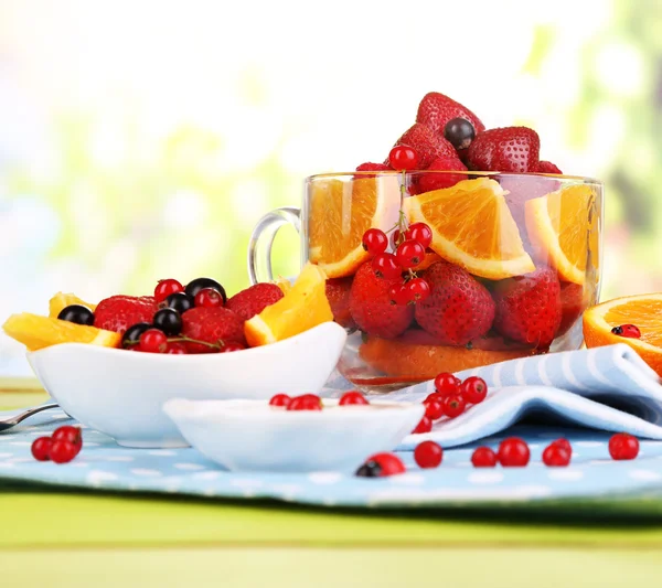 Užitečné ovocný salát ve sklenici a misku na dřevěný stůl na přírodní pozadí — Stock fotografie