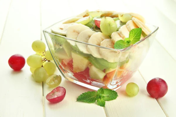 Ensalada de frutas sabrosas en cuenco de vidrio, sobre mesa de madera blanca — Foto de Stock