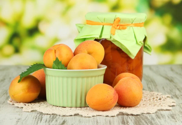 Apricot jam in glass jar and fresh apricots, on wooden table, on bright background — Stock Photo, Image