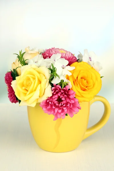 Beautiful bouquet of bright flowers in color mug, on wooden table, on light background — Stock Photo, Image