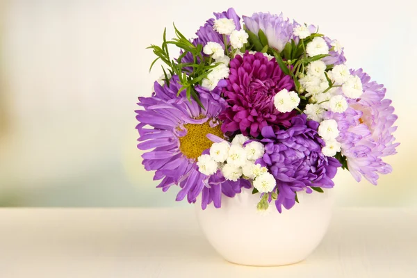 Beau bouquet de fleurs lumineuses en vase de couleur, sur table en bois, sur fond lumineux — Photo