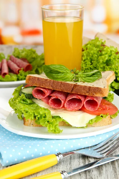 Composição com suco de frutas e saboroso sanduíche com salsicha de salame e legumes em guardanapo de cor, em fundo de mesa de madeira — Fotografia de Stock
