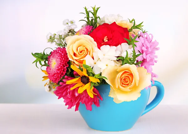 Beautiful bouquet of bright flowers in color mug, on wooden table, on light background — Stock Photo, Image