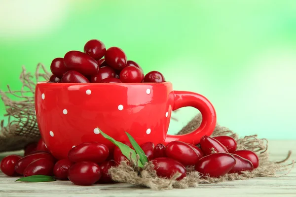 Fresh cornel berries in red cup on wooden table — Stock Photo, Image