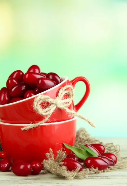 Fresh cornel berries in red cups on wooden table — Stock Photo, Image