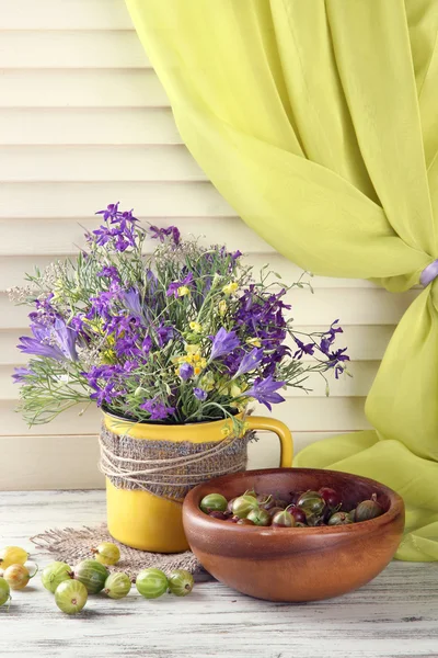Beau bouquet de fleurs sauvages en tasse et baies sur table en bois — Photo
