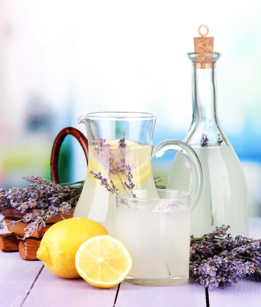 Лавандовый лимонад в стеклянной бутылке и кувшине, на фиолетовом деревянном столе, на ярком фоне — стоковое фото