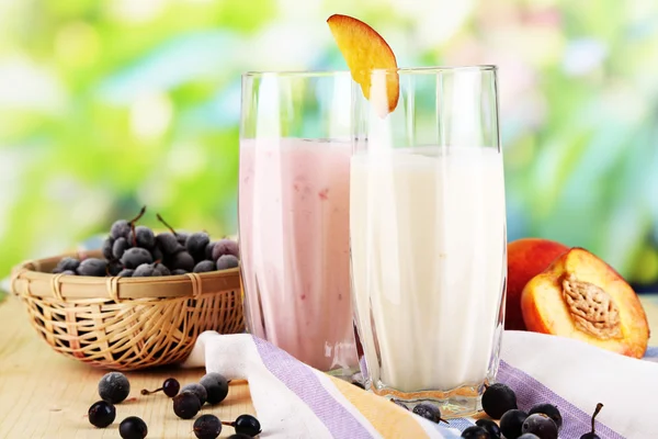 Deliciosos batidos de leche con mora y melocotón sobre mesa de madera sobre fondo natural — Foto de Stock