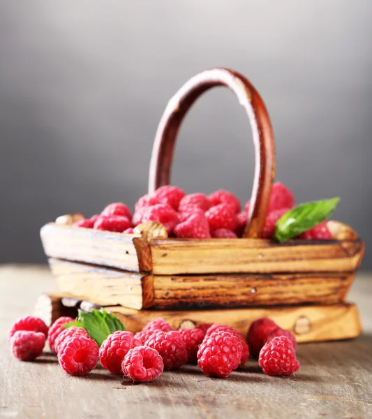 Ripe sweet raspberries in basket on wooden table, on grey background — Stock Photo, Image