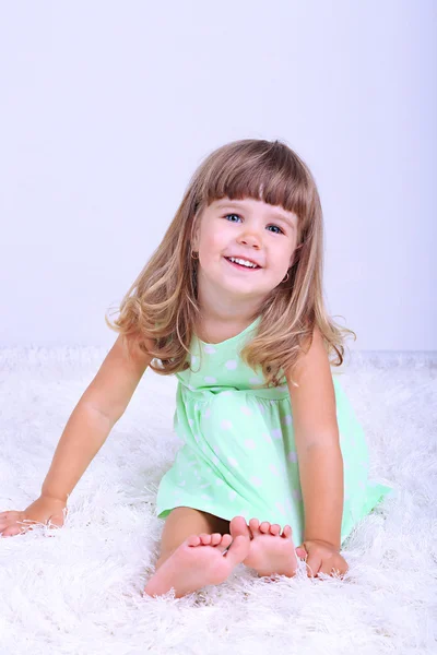 Little cute girl sitting on carpet, on gray background — Stock Photo, Image