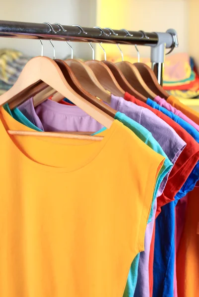 Variedade de camisetas casuais em cabides de madeira em prateleiras fundo — Fotografia de Stock