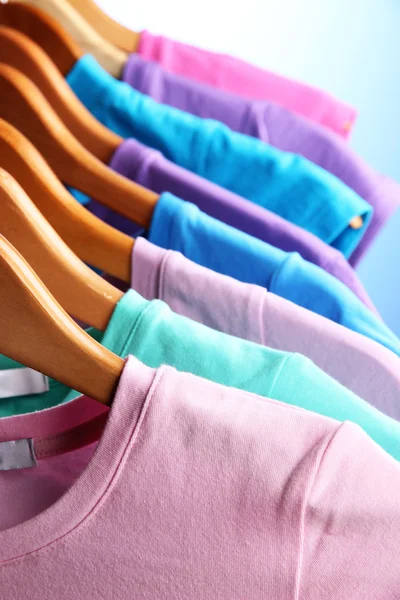 Un sacco di T-shirt su appendini su sfondo blu — Foto Stock