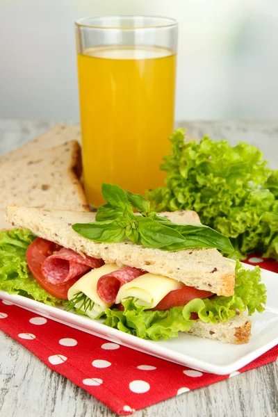 Lezzetli sandviç salam sosis ve parlak zemin üzerine ahşap masa üzerinde renkli peçete üzerinde sebze ve meyve suyu ile kompozisyon — Stok fotoğraf