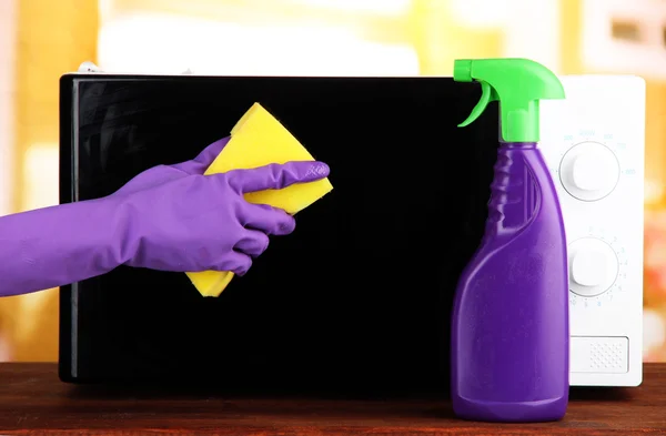 Ręka z gąbki do czyszczenia kuchenka mikrofalowa, na jasnym tle — Zdjęcie stockowe