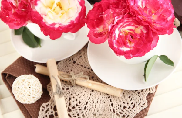 Roses in cups on napkins on wooden background — Stock Photo, Image