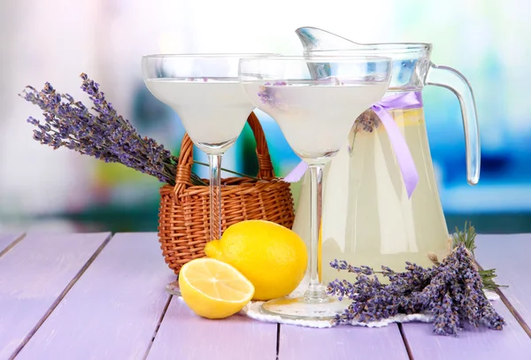 Lavender lemonade in glass jug and cocktail glasses, on bright background — Stock Photo, Image