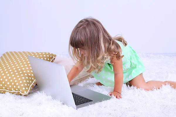 Lilla söta tjejen sitter på mattan med laptop, på grå bakgrund — Stockfoto