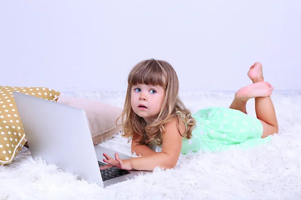 Pequena menina bonito encontra-se no tapete com laptop, no fundo cinza — Fotografia de Stock